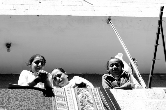 A mother tries to hide to avoid the picture, while her two daughters pose happily on their balcony in Jabal Amman